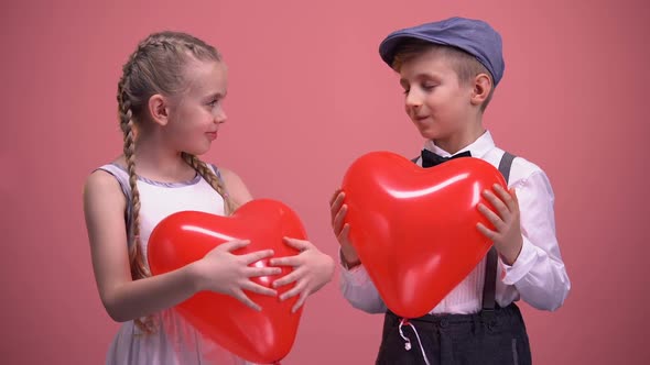 Cheerful Kids in Love Holding Red Heart-Shaped Balloons and Smiling to Camera