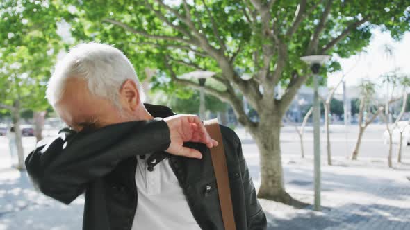 Caucasian man out and about in the city streets covering his mouth while sneezing