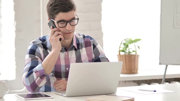 Positive Young Man Talking on Phone at Work