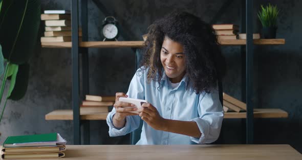 Young Concentrated Positive African American Woman Using Smartphone Sitting at Office Desk Playing