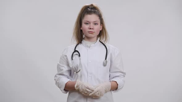 Pretty Caucasian Brunette Girl in Medical Gown and Gloves Showing Thumb Up Looking at Camera Smiling