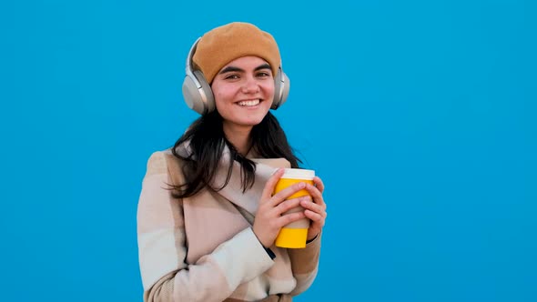 Woman with Headphones and Paper Cup Looking at Camera