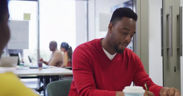 African american male and female business colleagues talking and taking notes in office