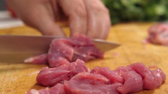 Closeup of a Cook Cutting Meat with a Knife on a Kitchen Board