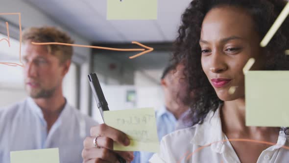 Professional businesswoman sticking memo notes on glass-board in modern office in slow motion