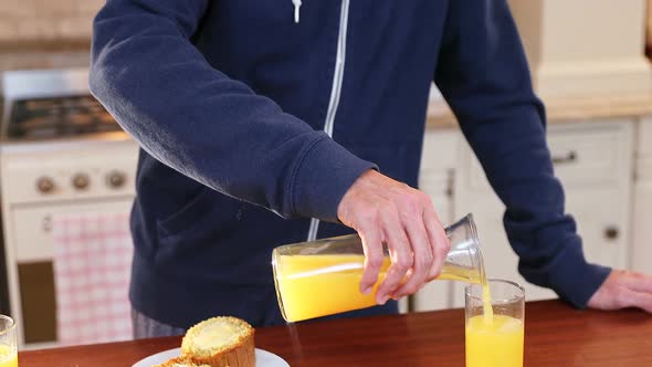 Man pouring juice into glass and having it in the kitchen