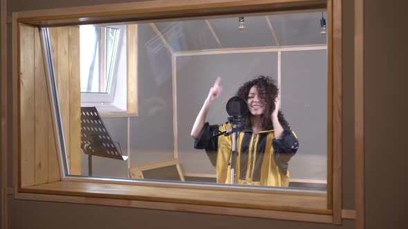 A Woman Artist Sings Behind Glass in a Recording Studio