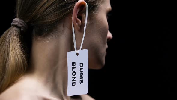 Determined Female Tearing Dumb Blond Label From Ear, Protesting Against Sexism