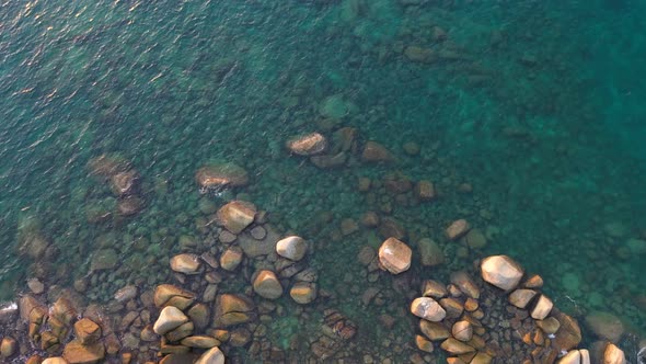 Aerial Top View Waves Hit The Rock Beach In Green Sea.