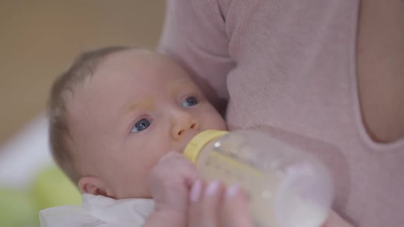 Closeup Carefree Happy Infant Eating Formula From Baby Bottle Lying in Hands of Woman