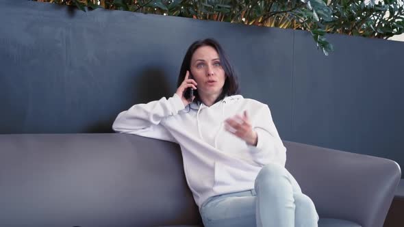 Smiling Young Business Woman of European Appearance in a White Sweater Sits in a Cozy Green Place in