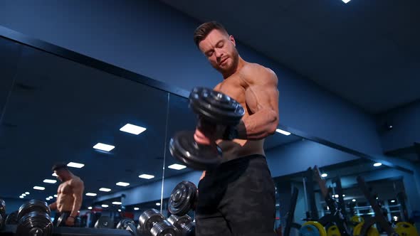 Handsome bodybuilder trains with dumbbells in modern gym. Slow motion