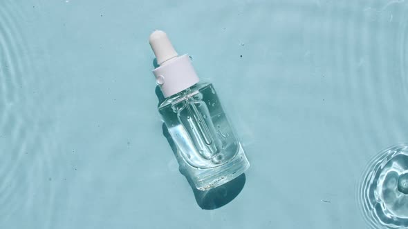 Glass Cosmetic Bottle with Pipette Lies on the Surface of the Water