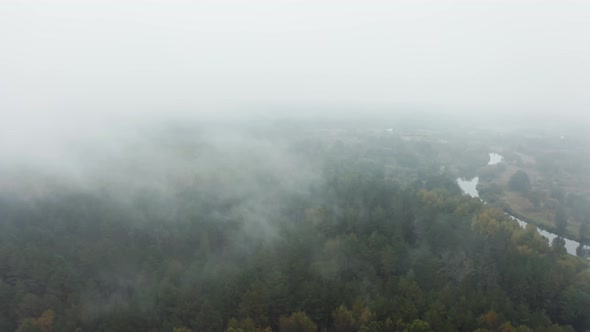 Drone Flies Through Rain Clouds Moving Over Fall Colors Treetops of Woodland and Winding River