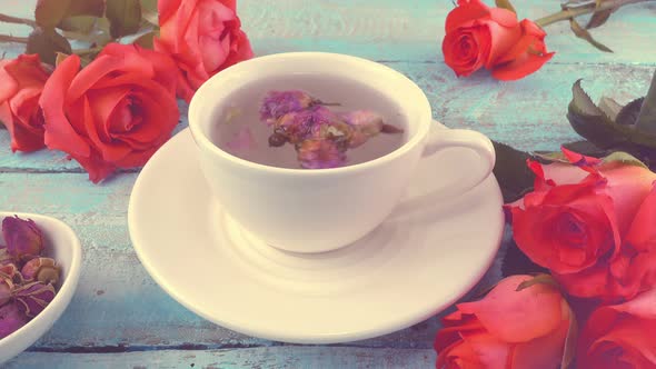White cap of  tea with fragrant dried rose buds, fresh rose flowers. Tea brewing.