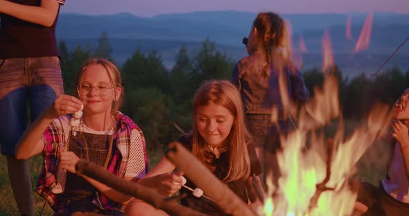 Group of Children Sitting Near Campfire Roasting Marshmallows at Campsite