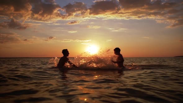 Silhouettes of Two Happy Boys 1012 Playing and Splashing Water While Swimming in Sea During