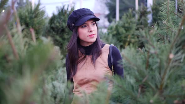 A hispanic woman in the holiday spirit shopping for festive Christmas trees.