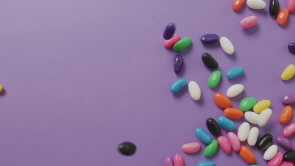 Video of overhead view of multi coloured sweets falling over purple background