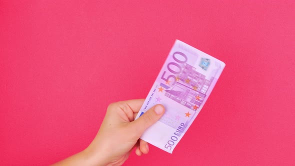 Hand in holds 500 EURO money bill on pink color background Counting cash european banknote exchange