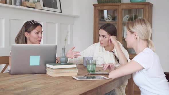 Friends are smiling, sitting at home at the table and talking about a new project, drinking tea 