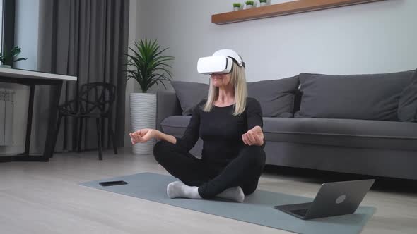 an Elderly Woman in Virtual Reality Glasses Meditates in the Living Room Modern Technology and