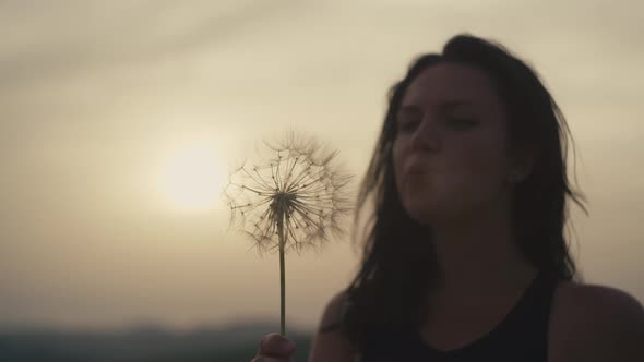 Slow Motion Video of a Girl Blowing a Dandelion in the Mountains at Sunset