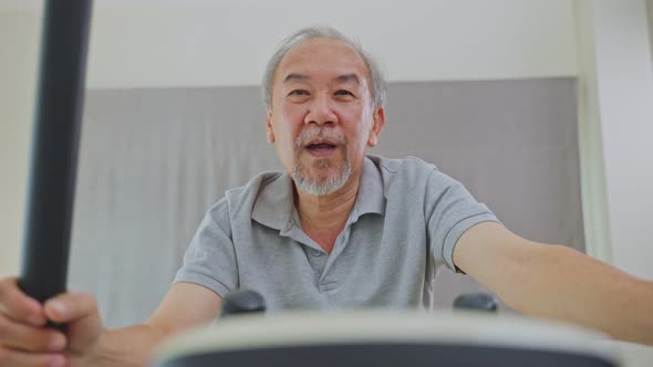 Asian Senior Elderly man workout cardio on cycling exercise bike machine at home for well being.