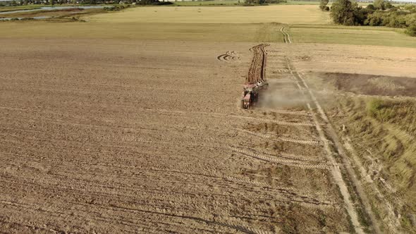 Powerful Tractor with a Plow Cultivating the Field and Raising Huge Clouds of Brown Suffocating Dust