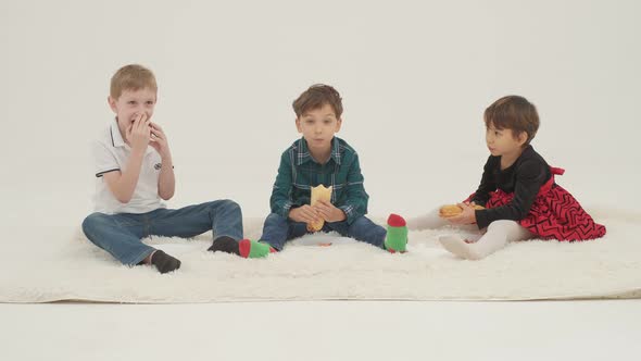 Three Children Eat Sitting on the White Fur Carpet