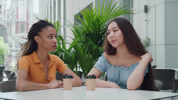 Young Mixed Race Girl with Dreadlocks and Attractive Asian Girl Sit at a Table and Have Cute