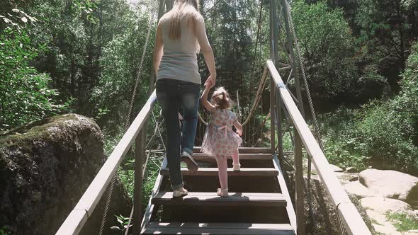 Young Beautiful Mother Rises a Little Child on a Wooden Bridge Across the River in the Forest