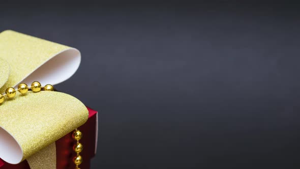 Red Gift Box with Gold Ribbon and Bow with Gold Beads on a Black Background