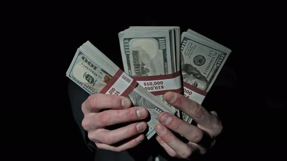 Three Stacks of 10000 American Dollars Bundles in Male Hands on Black Background