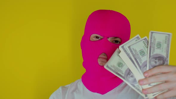 Close Up of Man in Pink Balaclava with Money and Gun on Yellow Background