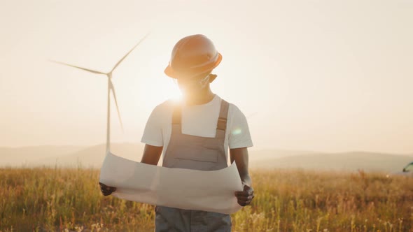 Focused African American Man with Blueprints in Hands Standing Among Farm with