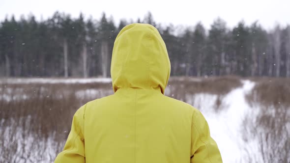 A man in a yellow jacket walks across a field in snowy weather