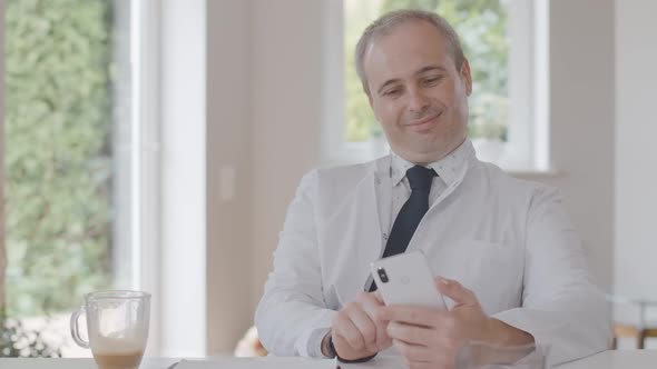 Smiling Male Doctor Surfing Internet on Smartphone. Portrait of Happy Mid-adult Caucasian Man