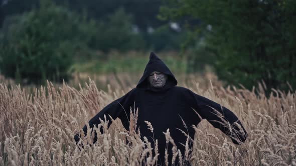 Mystical devil in black mantle on field. Portrait of a spooky figure with scary face in dark robe