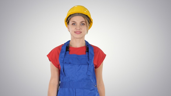 Young woman in yellow hardhat walking on gradient background.