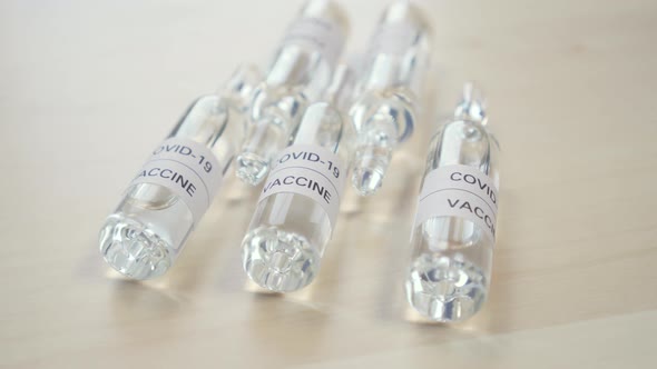 Five medical glass ampoules with a coronavirus vaccine on a wooden surface
