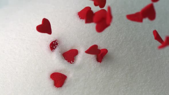 Red candy hearts fall atop stack sugar granules, Slow Motion