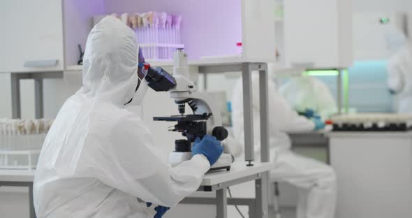 Scientist in Ppe Looking Into Microscope Conducting Research in Laboratory