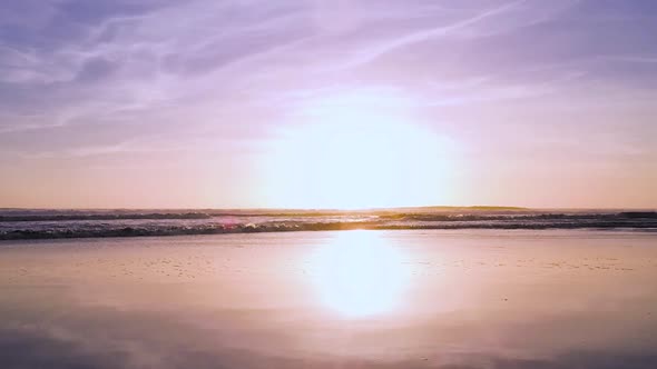 A stunning and beautiful purple sunset at the ocean as the waves roll in slow motion.