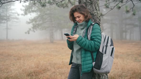 A Young Woman Typing a Message on the Phone While Leaning Against a Tree