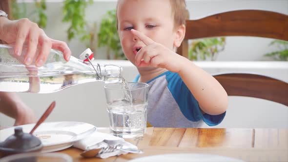 Mom Pours Water To His Son in a Glass and a Cute Child Drinks a Glass of Water. Child Is Drinking a