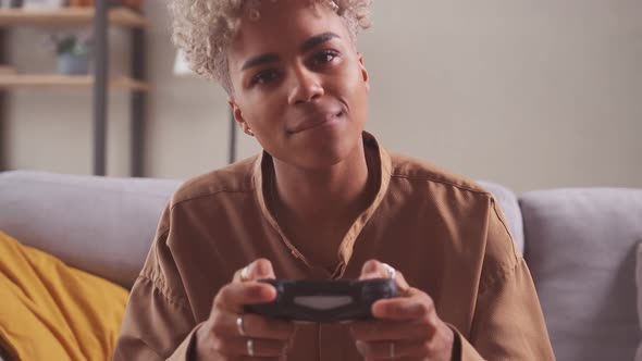 African Woman Player Sit on Couch Cross Legged at Home Holding Console Game Pad
