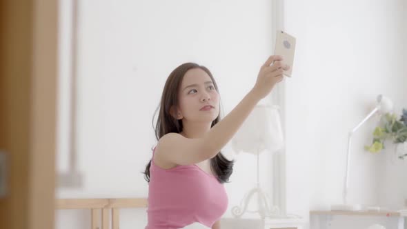 Beautiful young asian woman sitting taking a selfie with smart phone on bedroom.