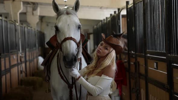 Ranch with Horses Young Woman is Holding Reins of White Calm Equine in Stable