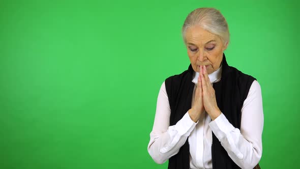 An elderly woman prays with hands clasped together - green screen studio